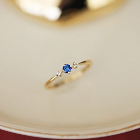 Vooraanzicht van de vergulde geboortesteenring van september met blauwe en witte cubic zirconia.