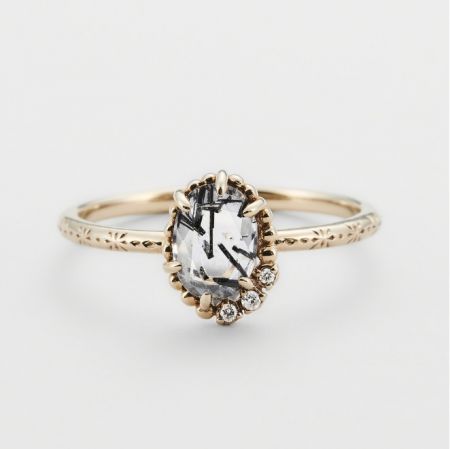 Anello in pietra preziosa sale e pepe in argento sterling 925 - Primo piano di un anello in pietra preziosa sale e pepe in argento sterling 925 con finitura dorata, che mostra il complesso motivo floreale inciso sulla fascia e le uniche inclusioni all'interno della pietra centrale.