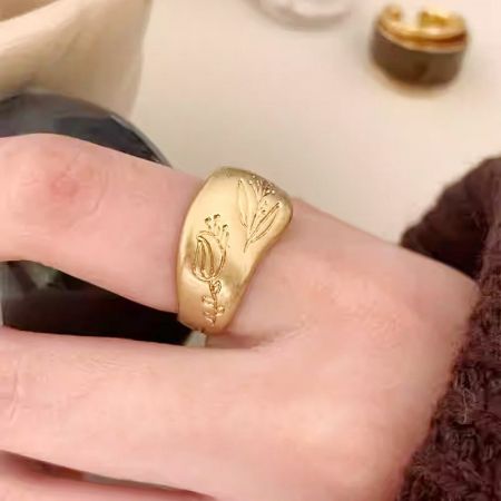 Close-up of a gold chunky ring with floral engraving worn on a finger.