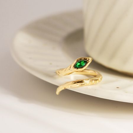 Vue détaillée d'une bague en or avec une pierre précieuse verte vibrante dans un cadre en forme de feuille.