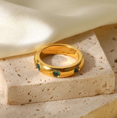Close-up van een vergulde roestvrijstalen ring met drie groene edelstenen.
