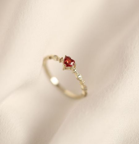 Anello a Forma di Cuore Rosso in Argento Sterling 925 - Un primo piano dell'anello a forma di cuore rosso in argento sterling 925 con finitura dorata, caratterizzato da una vivace pietra preziosa rossa a forma di cuore circondata da zirconia cubica scintillante su una fascia regolabile.
