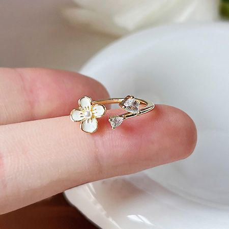 Close-up of a gold open-finger ring with a white flower and two brilliant zircon stones.
