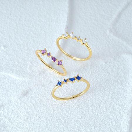 Set di anelli impilabili con quattro zirconi in argento sterling 925 (Set di 5) - Un set di tre anelli impilabili in argento sterling 925 con finitura dorata, ciascuno adornato con una fila di quattro zirconi in viola, blu e bianco.