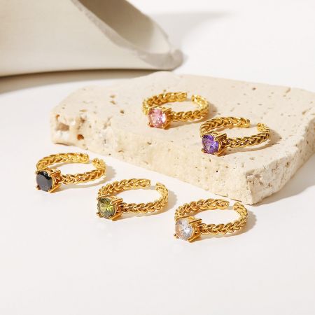 Anelli aperti in zirconia cubica in acciaio inossidabile placcato oro (set di 5) - Un set di cinque anelli aperti in acciaio inossidabile placcato oro, ciascuno con una gemma in zirconia cubica di colore diverso, esposti su uno sfondo bianco pulito.