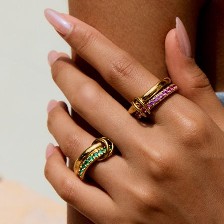A model's hand displaying two stackable gold rings from the set, one with pink and one with green cubic zirconia.