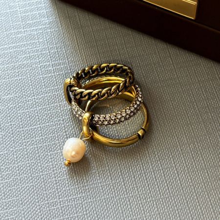 Wholesale Brass Rings Collection - A stylish collection of wholesale brass rings from JR Fashion Accessories, featuring a set of three gold-toned rings with a delicate pearl pendant.