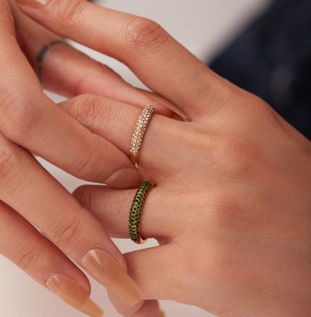 Close-up van twee gouden gelaagde ringen, één met witte en één met groene cubic zirconia stenen.