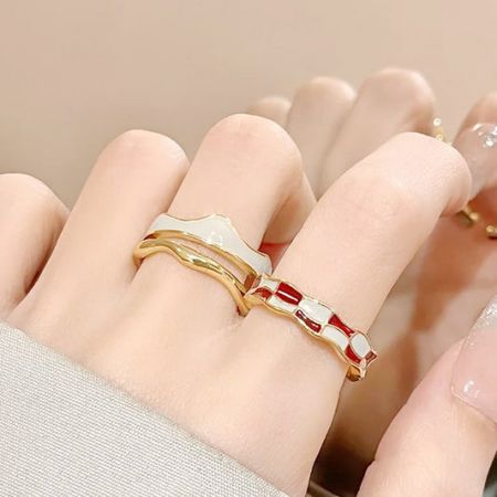 Close-up van een hand met vergulde emaille ringen met een modern dambordontwerp.