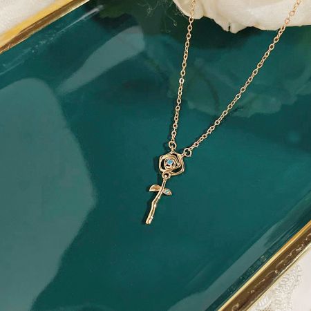 Close-up of the gold rose pendant necklace on a dark teal tray, highlighting the intricate details.