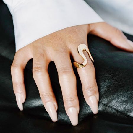 A mão de uma mulher usando um anel geométrico em forma de S dourado do conjunto de aço inoxidável.