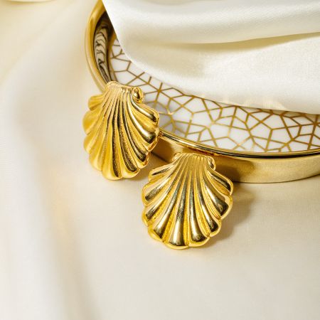 The gold shell earrings presented on a stylish white and gold geometric patterned dish.
