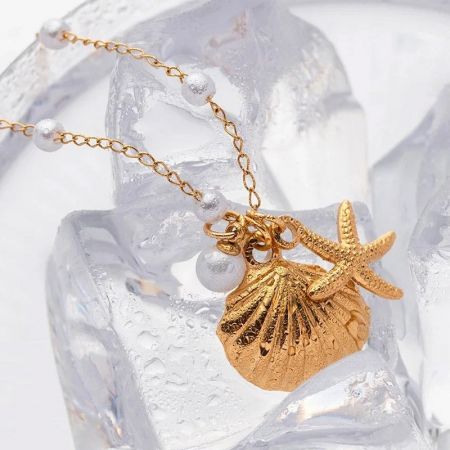 Conjunto de Collar de Cadena con Perla y Colgante de Concha de Estrella de Mar de Joyería de Playa de Acero Inoxidable - Una toma de estudio detallada de un collar de acero inoxidable dorado con un delicado colgante de concha de mar y estrella de mar, parte de un conjunto de joyería con temática de playa.