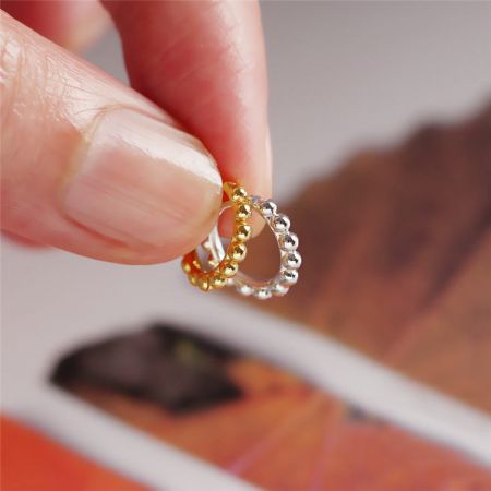 Una mano che tiene un orecchino a cerchio con perline dorate e uno argentato per confrontare le finiture.