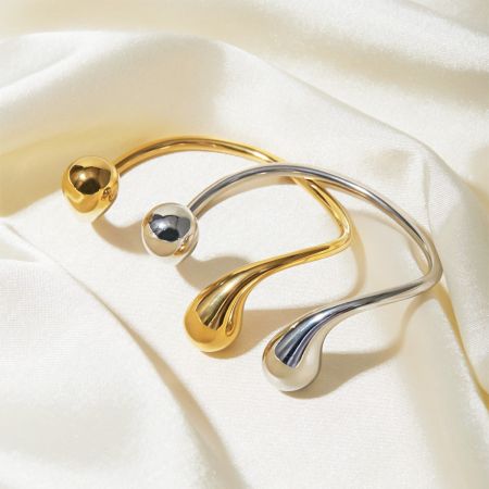 Close-up van de gouden en zilveren asymmetrische cuff bangles op een witte stof achtergrond.