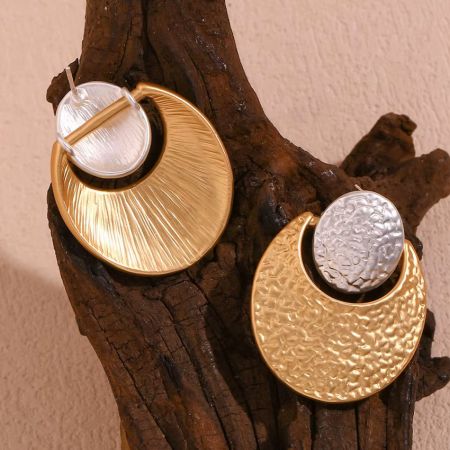 A pair of gold and silver geometric earrings showcased on a driftwood piece.