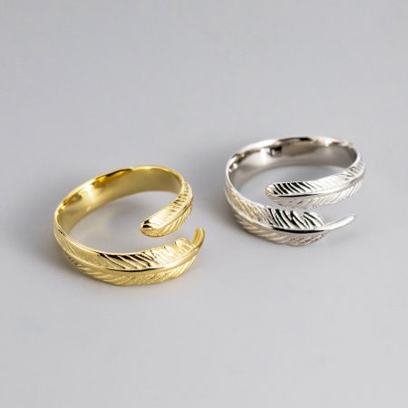 Anelli a forma di piuma regolabili per donne set di 5 in argento sterling 925 - Una coppia di anelli a forma di piuma regolabili in argento sterling 925, uno con finitura argentata lucida e l'altro con finitura dorata radiosa, esposti fianco a fianco.