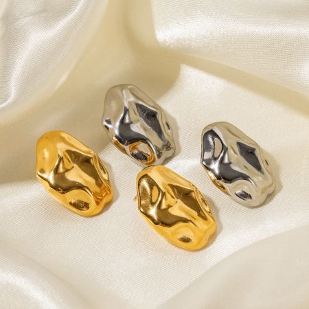 Los pendientes irregulares de oro y plata exhibidos sobre una lujosa tela de satén.
