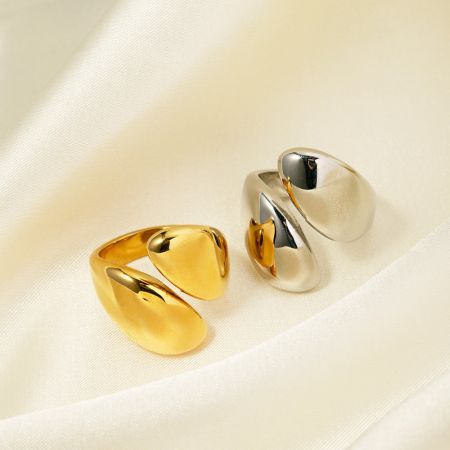 Close-up de dois anéis statement com um design torcido distinto, um em ouro e outro em prata.