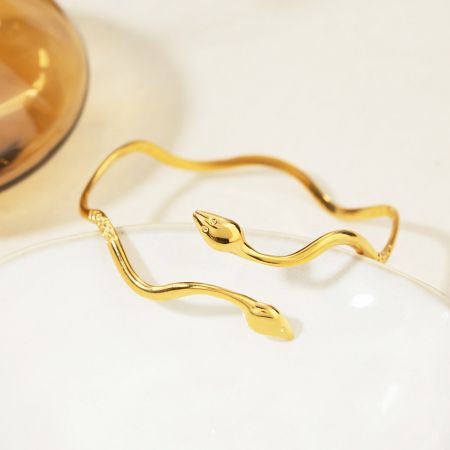 Roestvrijstalen golvende dubbelkopige slang open armband bangle set van 5 - Een gedetailleerde close-up van een gouden dubbelkopige slang open armband gemaakt van roestvrij staal, met een ingewikkeld golvend ontwerp en edelsteenogen.