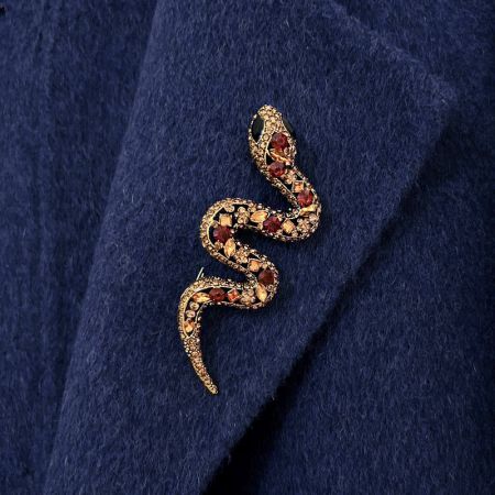 Gros plan d'une broche en or en forme de serpent avec des pierres précieuses rouges et noires vibrantes sur un tissu bleu foncé.