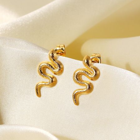 Bovenaanzicht van de gouden slang stud oorbellen op een crèmekleurige stof.