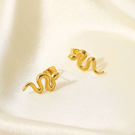 Gedetailleerd uitzicht op de gouden slang oorbellen op een crèmekleurige satijnen achtergrond.