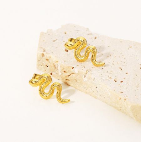 Pendientes de Stud de Serpiente Distorsionada Baño de Oro en Acero Inoxidable (Juego de 5 Pares) - Un par de pendientes de acero inoxidable chapados en oro exhibidos sobre una piedra beige texturizada, destacando su diseño distorsionado único.