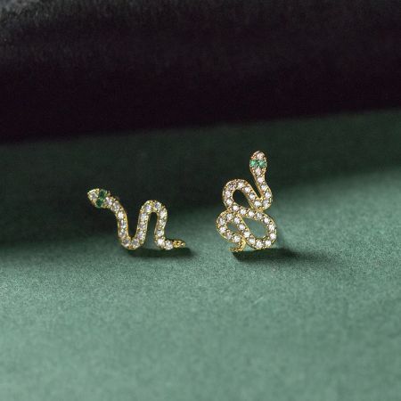 Eleganti orecchini a forma di serpente in oro adornati con pietre bianche e occhi in pietra verde vibrante.