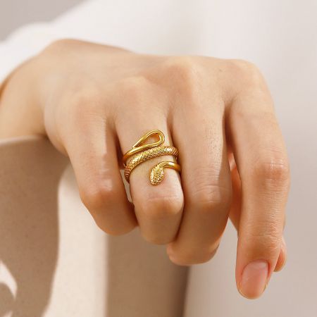 Een close-up van de gouden slangring die om een vinger wordt gedragen, met een gedetailleerd wikkeldesign.