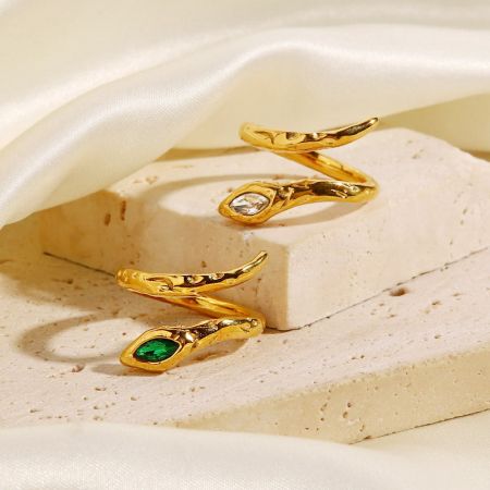 Gros plan de deux bagues en or en forme de serpent, l'une avec des pierres de zircon vert et l'autre avec des pierres de zircon blanches.