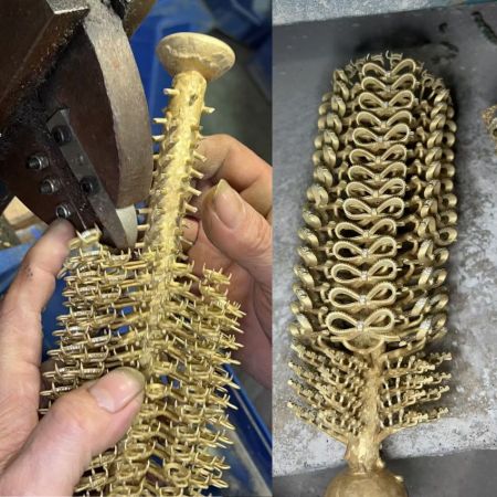 Ein kunstvoll gegossenes goldfarbenes Dekorationsstück mit einer wirbelsäulenartigen Struktur.