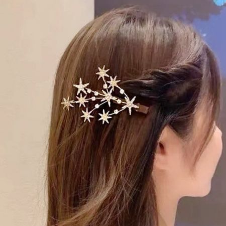 Un modello con lunghi capelli castani che indossa una clip per capelli a forma di stella di cristallo dorato e luccicante.