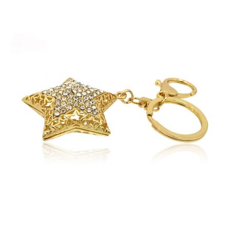 Vista detalhada do intrincado design de filigrana e incrustações de strass no chaveiro em forma de estrela dourada.