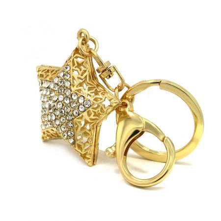 Llavero metálico personalizado con diseño de estrella dorada y strass. - Vista completa del llavero metálico personalizado con diseño de estrella dorada y strass, mostrando el colgante en forma de estrella con detalles de filigrana, el anillo para llaves y el cierre.