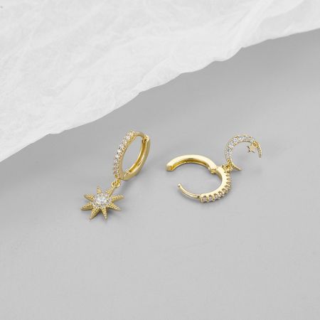 Otro ángulo de los pendientes de estrella y luna de oro con piedras preciosas claras sobre un fondo blanco.