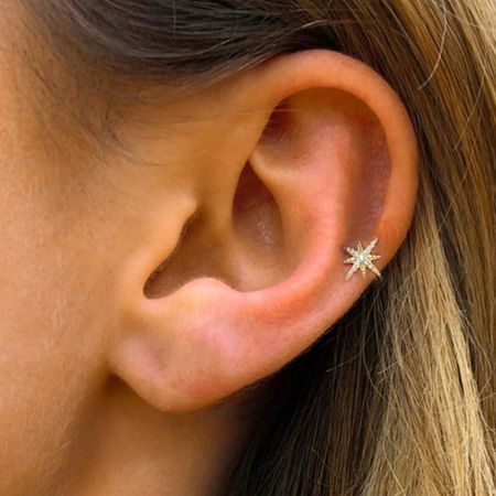 Primo piano di un orecchino a cuffia in zirconia dorata a forma di stella indossato su un orecchio.