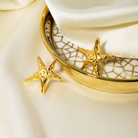 The gold star stud earrings presented on a decorative white plate, highlighting their luxurious finish.