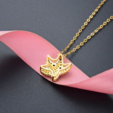 De elegante gouden zeesterhanger met een delicate geperforeerde ontwerp, getoond op een roze lint.