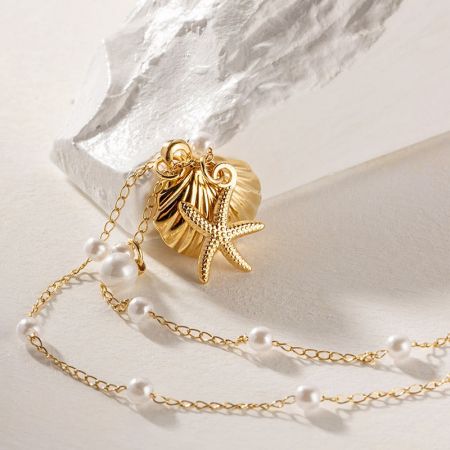 Ein schöner goldener Seestern- und Jakobsmuschel-Anhänger mit einer einzelnen Perle, der die filigranen Details zeigt.