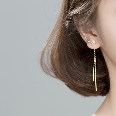 Model met de asymmetrische gouden franje- en parel oorbellen om schaal en stijl te tonen.