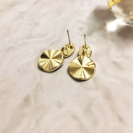 イヤリングの金メッキ真鍮部品にあるテクスチャーのあるサンバーストパターンのクローズアップ。