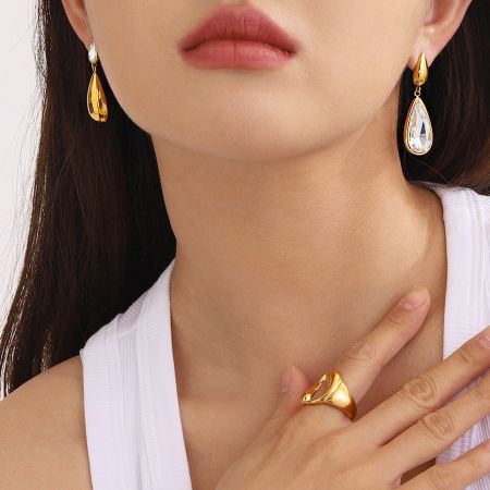 Gli orecchini a goccia d'oro esposti come parte di un set di gioielli coordinato con un anello.