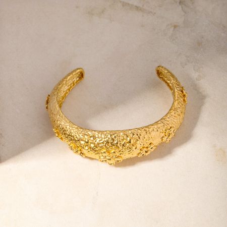 金色のカフバングルに施された複雑なハンマーテクスチャーと花のデザインの詳細なビュー。
