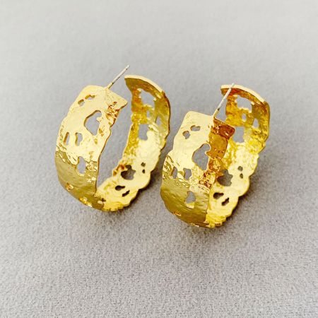 Primo piano dettagliato di un orecchino a cerchio a forma di C in oro placcato che mostra la sua superficie testurizzata e le perforazioni irregolari.