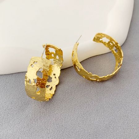 Un paio di orecchini color oro con un design testurizzato e organico, che mostrano il loro fascino unico e artistico.
