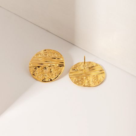 Close-up van de gouden hamerslag stud oorbellen met een gestructureerde, gepolijste afwerking.