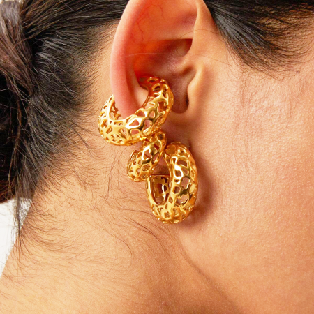 Toma de cerca del pendiente en forma de C chapado en oro en la oreja de un modelo, mostrando su escala y textura.