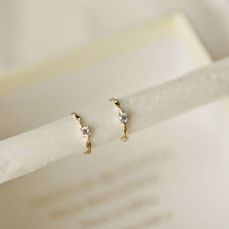 Pendientes huggie de aro retorcido dorado de plata esterlina 925 con zirconia al por mayor. - Un primer plano de un par de pendientes huggie de aro 925 de plata esterlina al por mayor con un diseño retorcido dorado, intrincadamente engastados con piedras de zirconia brillantes.