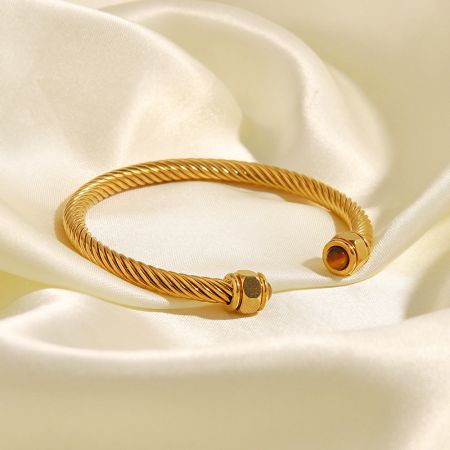 Ett enda guldpläterat vridet armband med eleganta stendetaljer, visat på en neutral bakgrund.